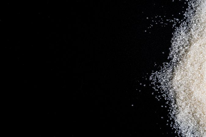 Flat lay of granulated sugar positioned on the right side over a dark background.