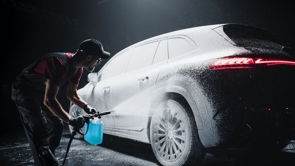 Professional Car Wash Specialist Spraying Smart Foam to Prepare a Modern Electric SUV with Contemporary Design for Sale at a Dealership Car Center.