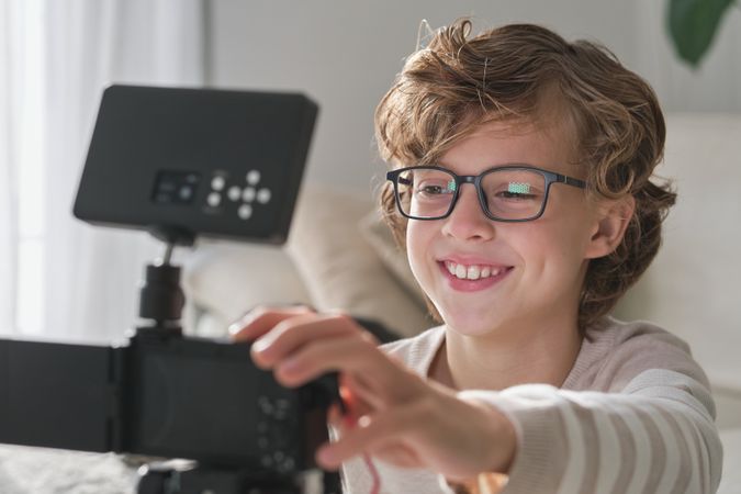 Positive boy setting up camera while recording video for blog