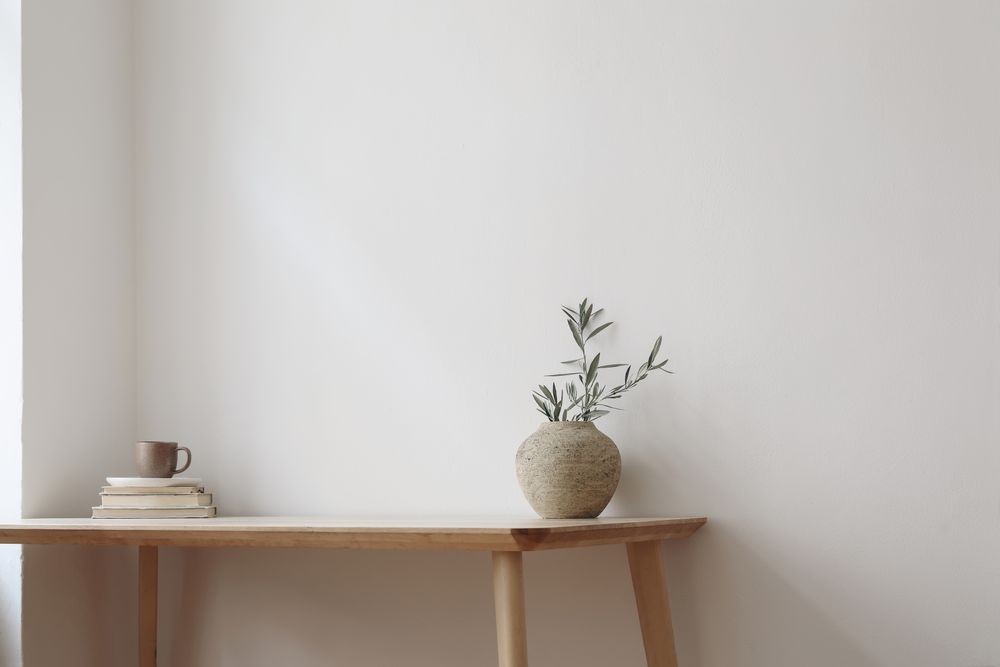 Wooden table with vase with eucalyptus branch and pile of books with mug