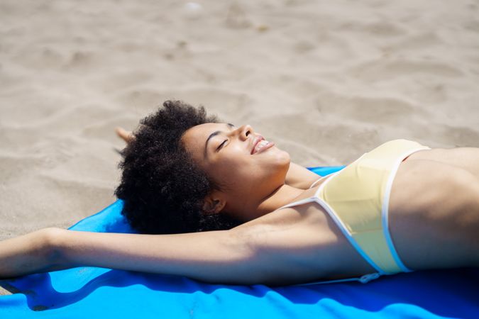 Female in yellow bikini relaxing on blue towel on the beach