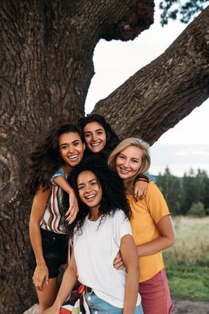 Four smiling woman posing in front of tree outside