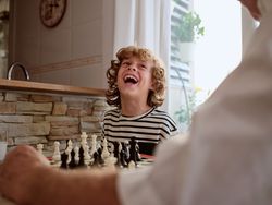 Delighted boy playing chess with unrecognizable grandparent