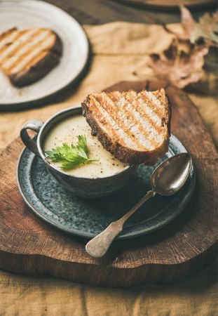 Celery soup in cup with toast, and spoon, on wooden board
