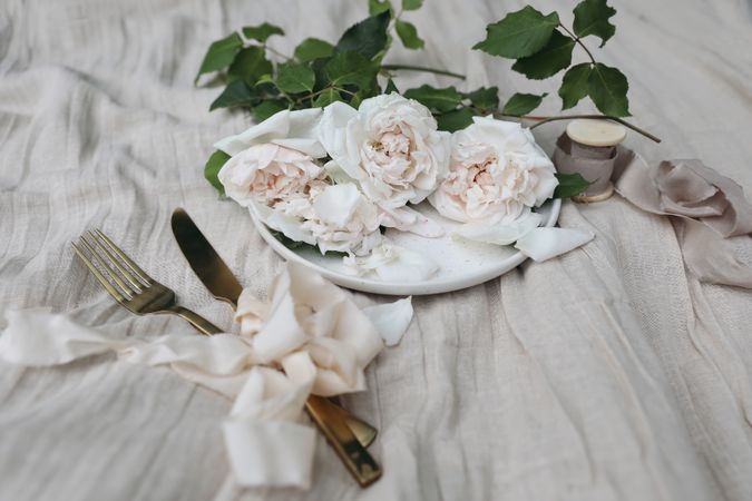 Plate, golden cutlery, delicate pink nude colored roses on beige linen tablecloth