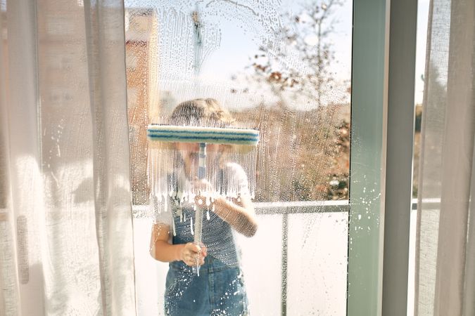 Unrecognizable boy washing windows at home