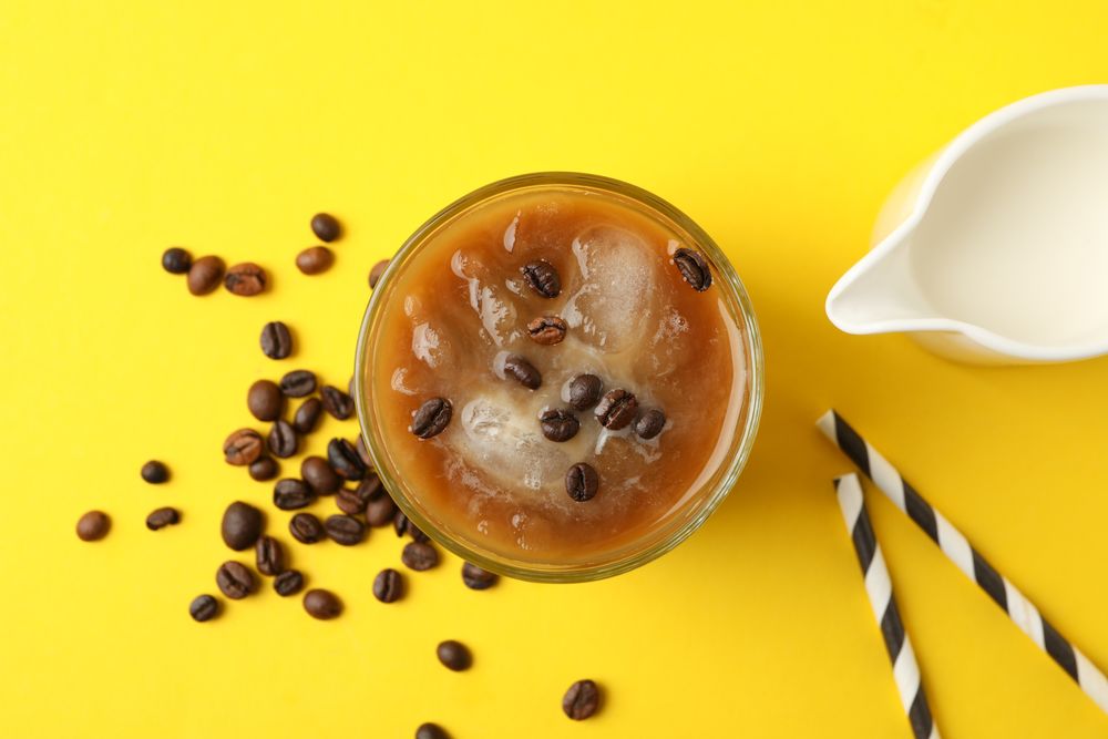 Glass of ice coffee on yellow background. Fresh drink