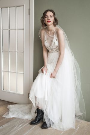 Adult confident woman in white dress and military shoes leaning on wall