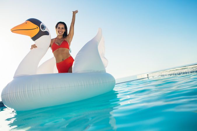 Excited female having fun sitting on an inflatable swan in a pool