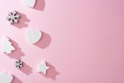 Wooden snowflakes hearts and Christmas tree decoration with pink background with shadows