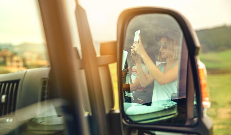 Rear view mirror of woman taking picture in vehicle