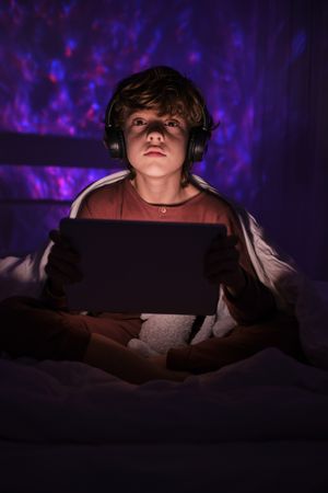 Focused boy with tablet in dark bedroom