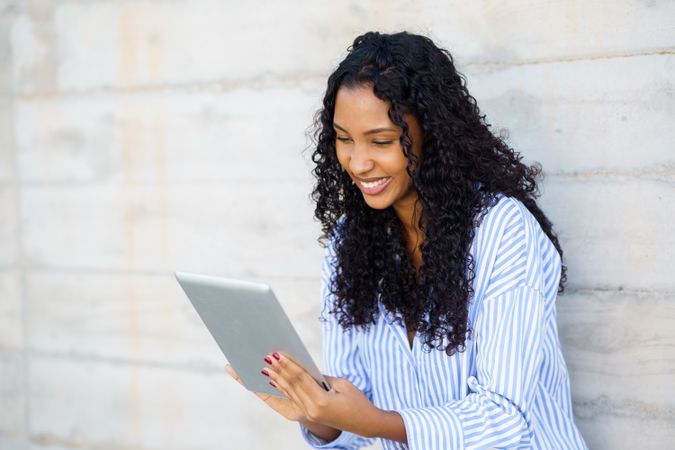 A joyful and happy young woman is utilizing a tablet device while being outdoors, enjoying her time