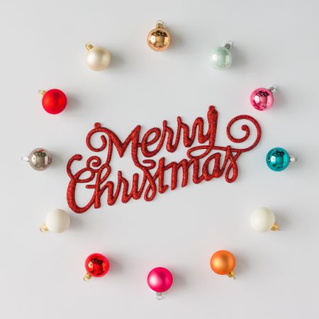 Circular border of colorful Christmas bauble decorations on light background with “Merry Christmas”