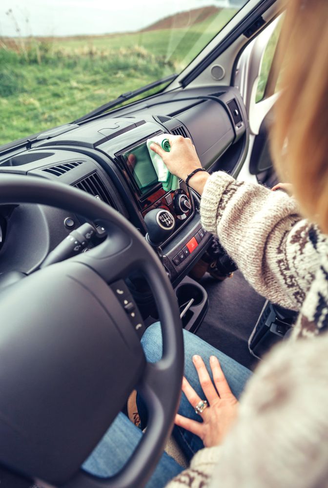 Female in warm sweater cleaning dashboard of parked vehicle