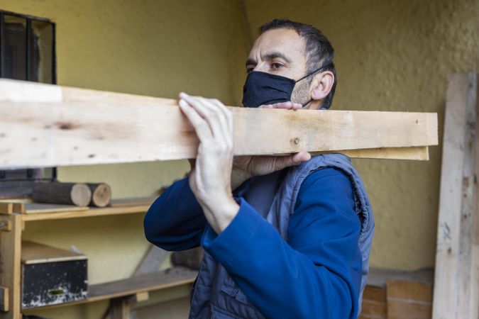 Man in blue shirt holding brown wooden plank