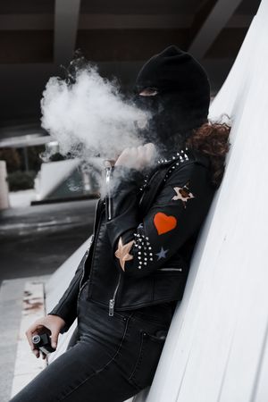 Woman in mask and jacket smoking on street
