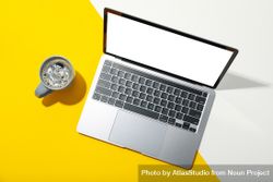 Laptop with mockup screen with mug of coffee on dual tone yellow background bejYE0