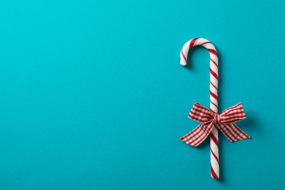 Sweet candy cane with bow on turquoise background, space for text