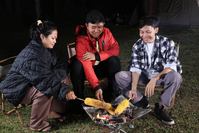 Group of Asian Young Male and Female  Grilling Corn on Campfire