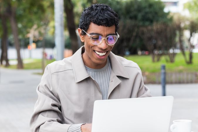 Happy hispanic male freelancer working on laptop in city