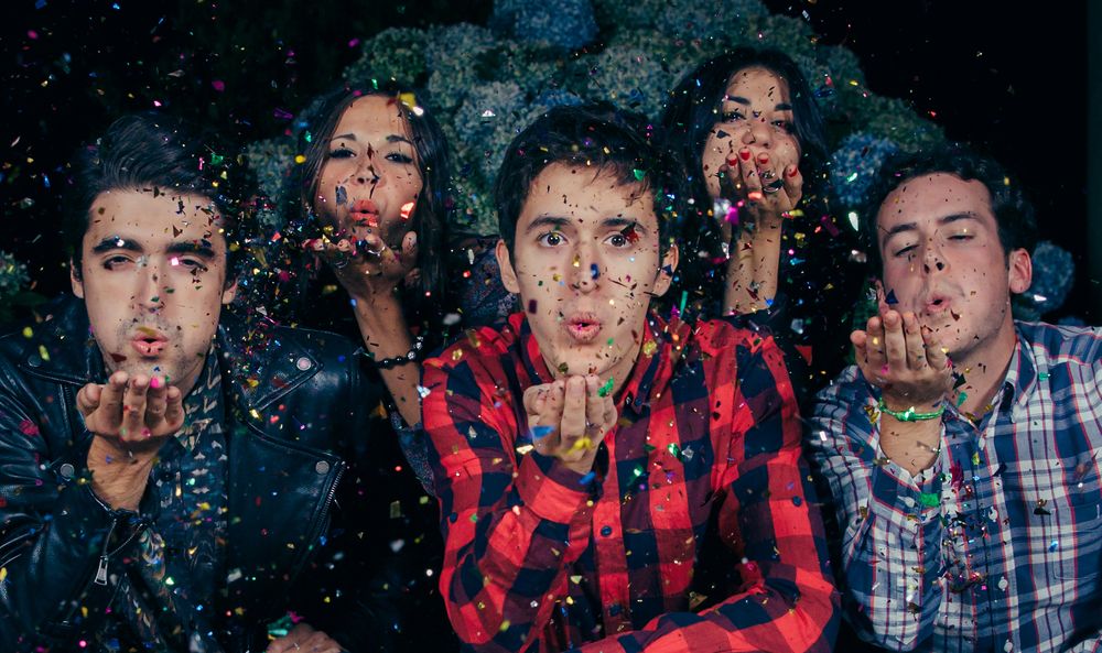Group of friends blowing confetti to the camera at a party