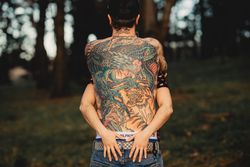 Young guy in tattoos hugging woman in forest