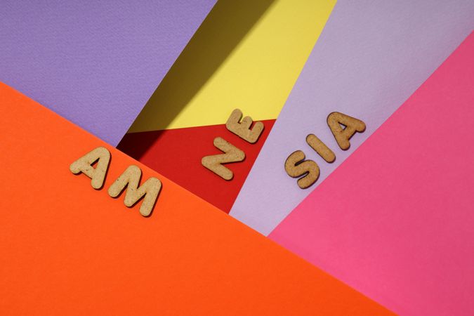 Scattered brown letters spelling “amnesia” on multi-colored paper background