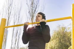 man doing pull-ups exercises on a crossbar in a public car