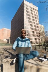 Stylish young Black man working remotely on laptop in city park