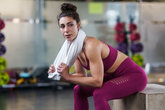 Side view of woman sitting in gym with towel around her neck