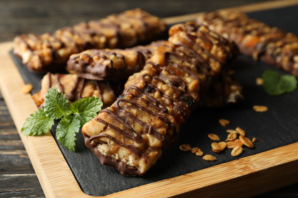 Board with granola bars on wooden background, close up