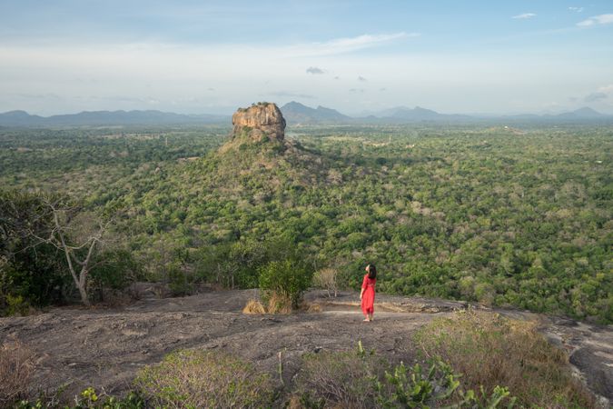 Tourist against solitary rock in middle of green forested plain under clear sky in summer