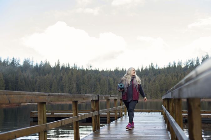 Woman walking on a lake dock while holding a rolled up yoga mat