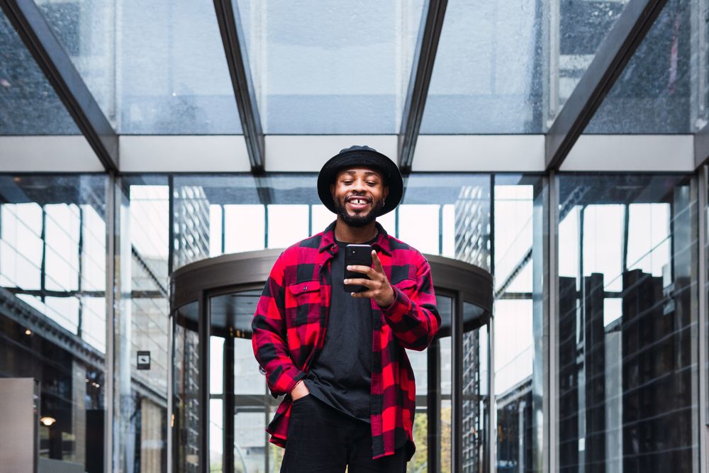 Cheerful Black male with smartphone in contemporary building