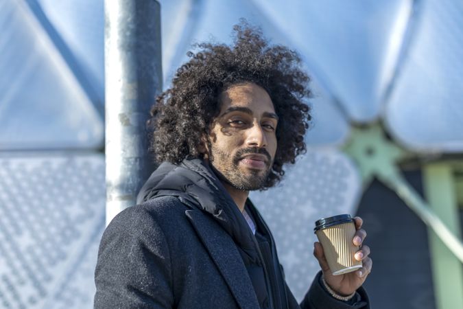 Black man in jacket with warm beverage standing outside