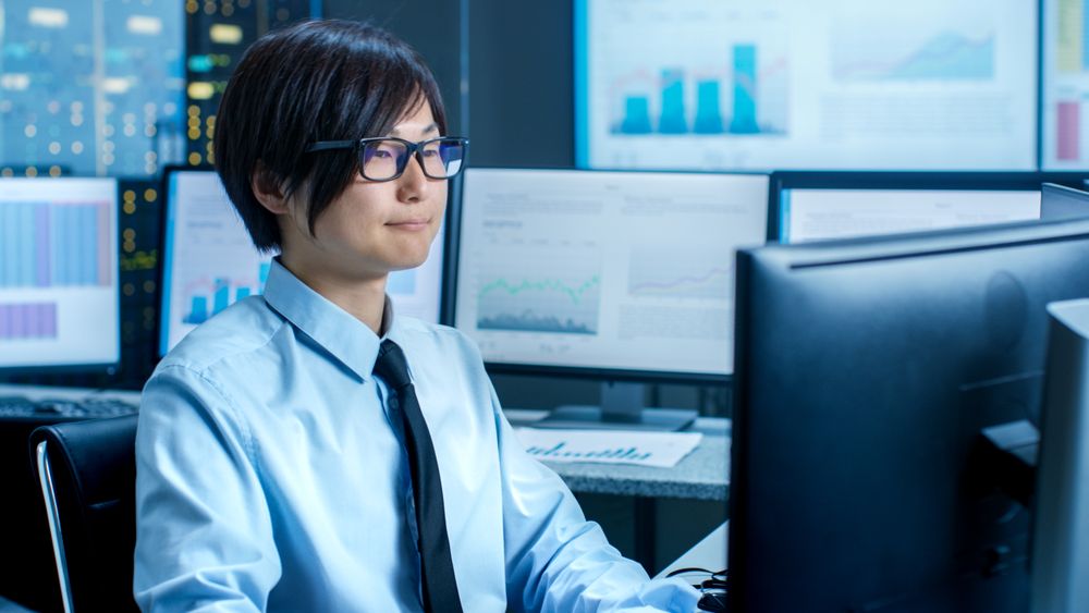 In the Data Mining Center Statistician sits at His Workstation Surrounded with Monitors Displaying Data and Graphs.