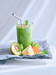 Green smoothie near cut fruits