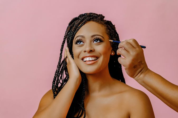 Female smiling and looking up while having make up applied in pink studio shoot