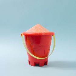 Sand castle bucket with spilled sand against pastel blue background