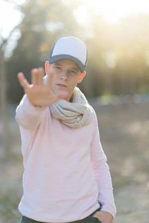 Teenage male wearing a cap with hand outreached saying "no"