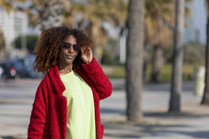 Female with hand to her sunglasses on street with palm trees