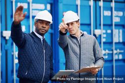 Two men in hard hats pointing towards a building project onsite 5oAkxb