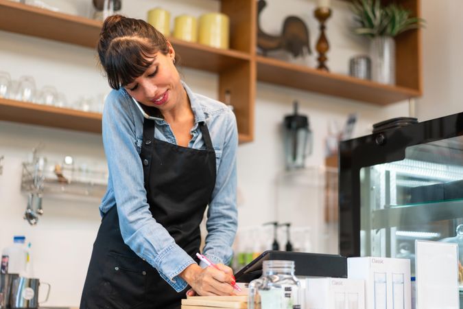 Female in apron working in cafe writing an order down from a phone call