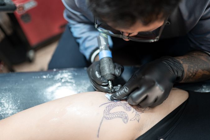A tattoo artist is tattooing a snake on a woman's leg