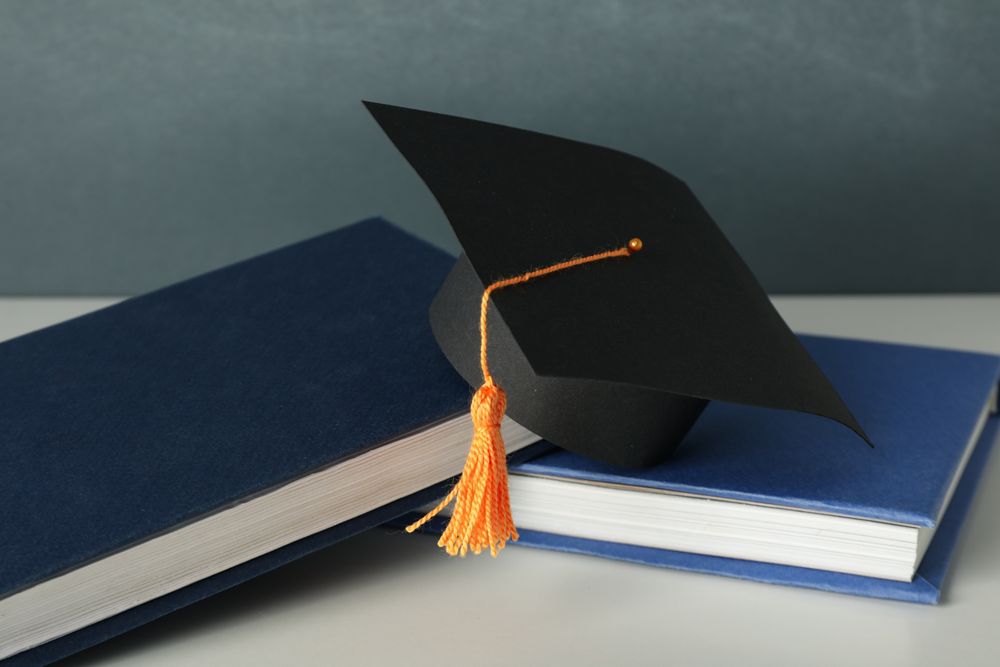 Graduation hat with books on a table on a dark background.