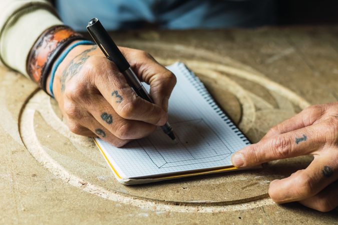 Crop woodworker drawing sketch in notebook