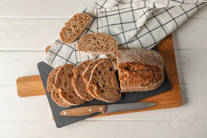 Composition with bread, knife, kitchen towel and cutting board on wooden background, top view and space for text