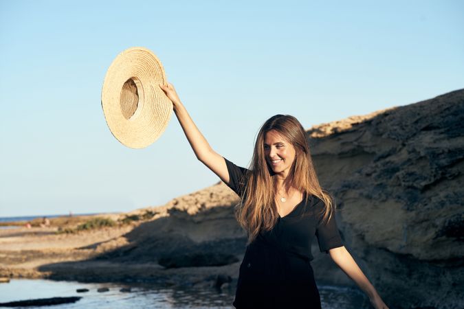Cheerful woman holding hat in air