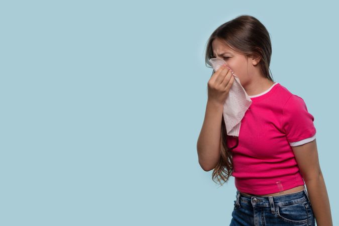 Girl sneezes into tissue, wearing pink shirt.